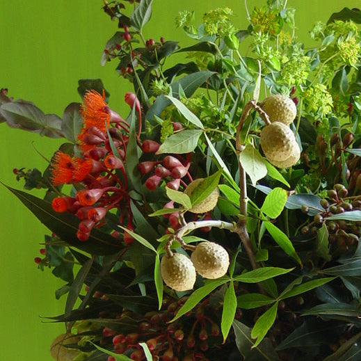 A large white stone-style urn filled with a lush artificial floral arrangement featuring green leaves, red berries, and light green hydrangea blooms, set against a bright lime green wall.