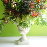 Floral arrangement in a decorative urn against a green background