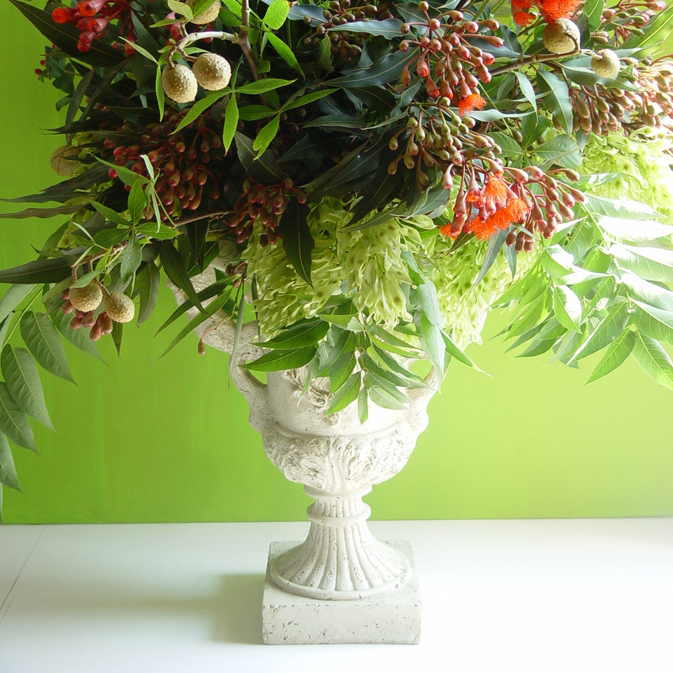 Floral arrangement in a decorative urn against a green background