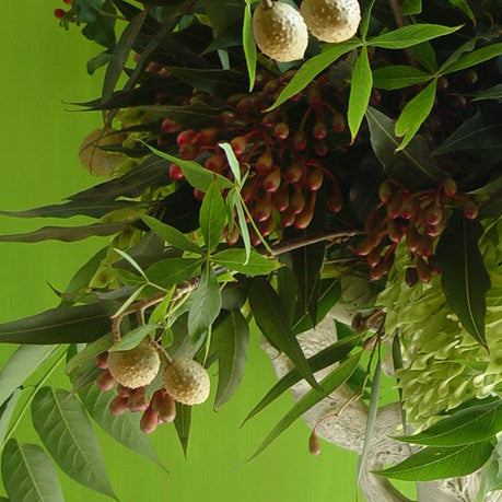 A large white stone-style urn filled with a lush artificial floral arrangement featuring green leaves, red berries, and light green hydrangea blooms, set against a bright lime green wall.